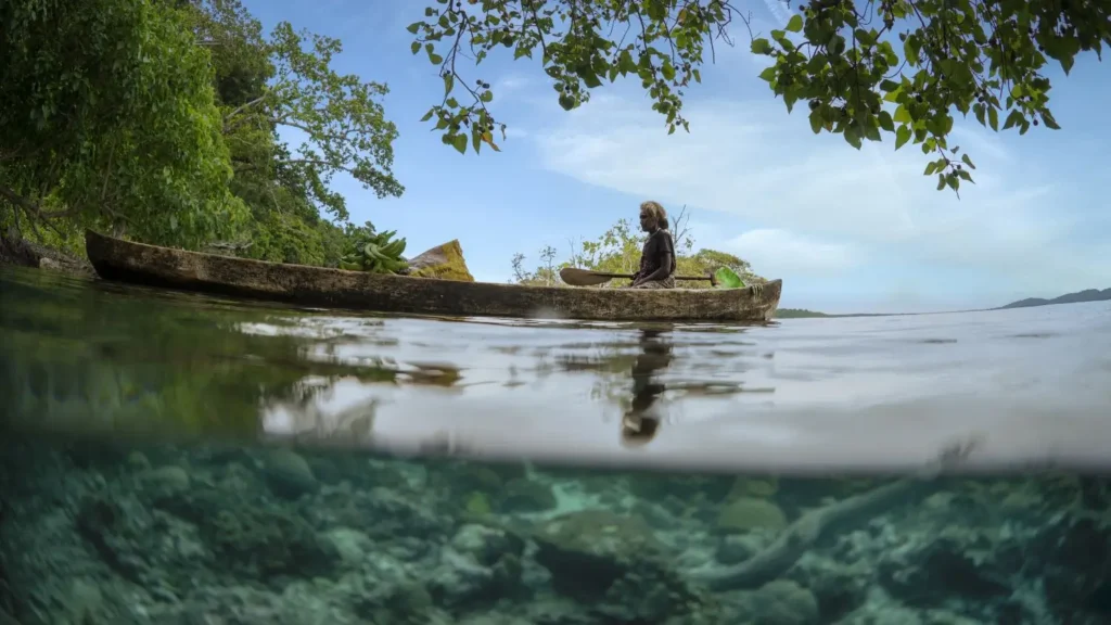 A split photo of a traditional Solomon Islands dugout canoe floating over a shallow reef.