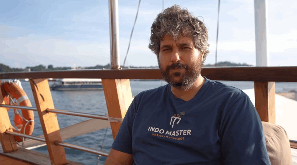 Guislain, cruise director and dive guide onboard Indo Master, smiling on deck with the ocean in the background.