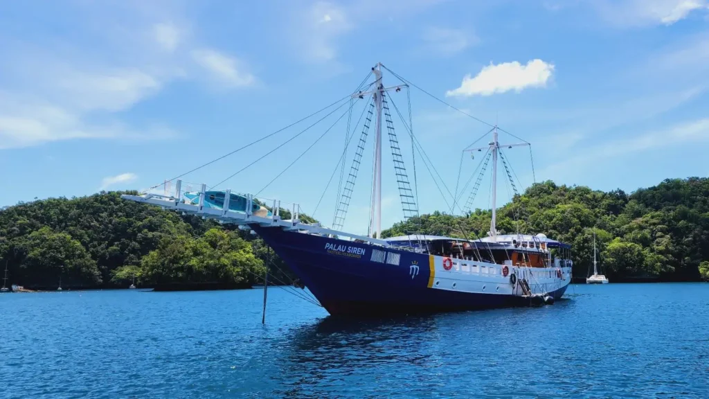 Palau Siren liveaboard moored in a calm emerald lagoon surrounded by limestone islands.