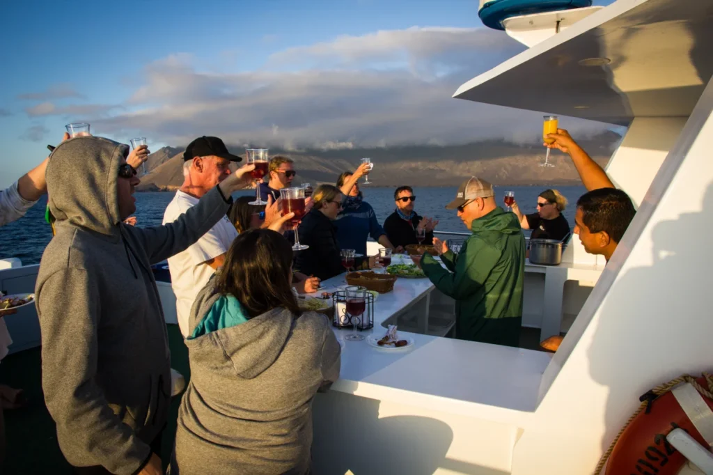 Relaxing during a liveaboard diving experience with divers holding cold drinks on the sundeck while watching a golden ocean sunset.