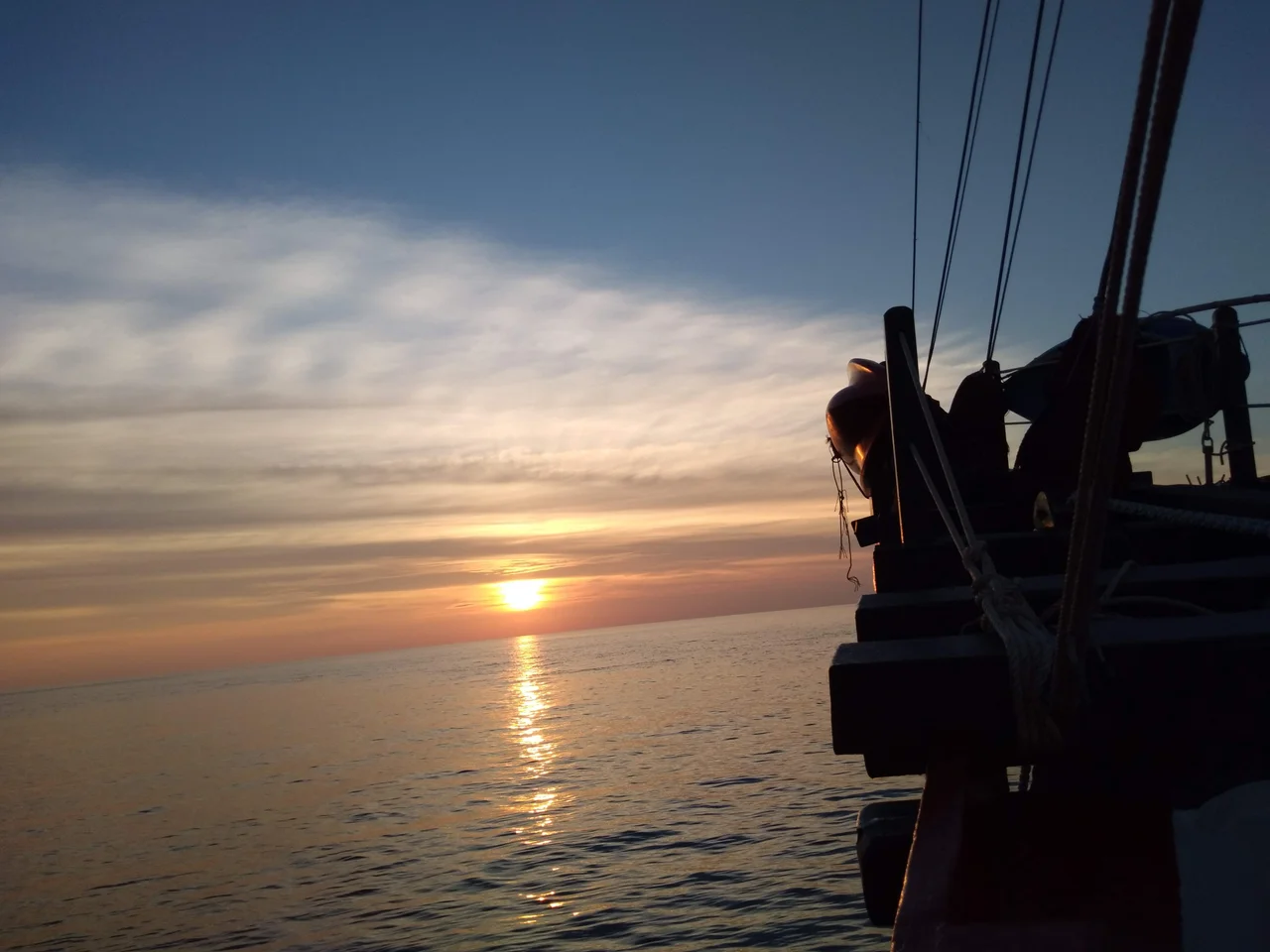 A diving liveaboard vessel anchored in calm tropical waters during a vibrant orange and pink sunrise, capturing a peaceful liveaboard diving experience.